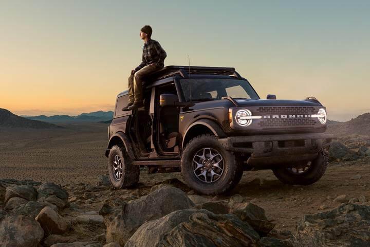 Man sitting on top of Ford Bronco in the desert