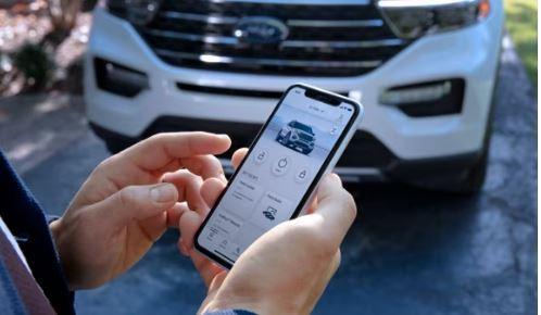 Hands holding a smartphone with the FordPass app open. Ford explorer in the background