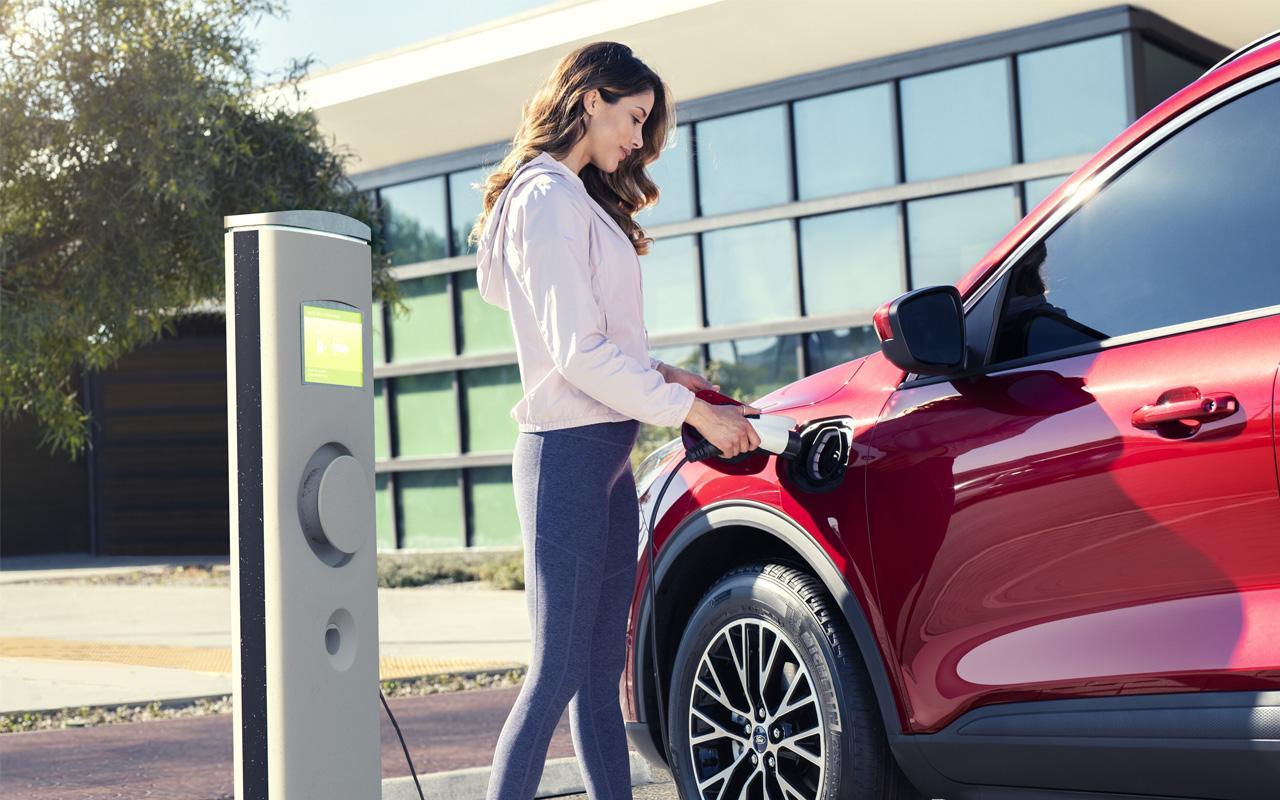 Woman plugging in her 2022 Ford Escape SE Hybrid at a electric vehicle charging station