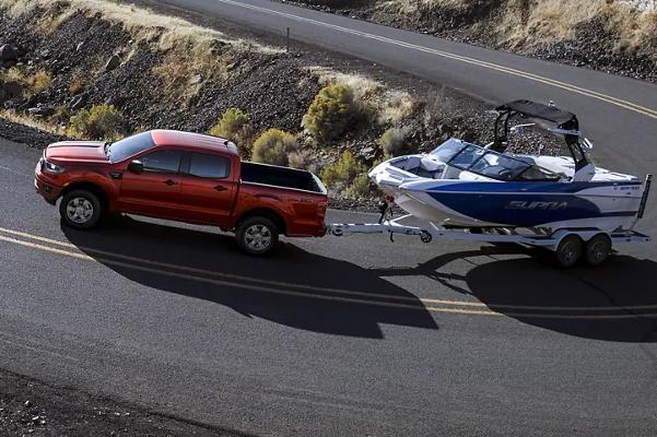 2022 Ford Ranger in Hot Pepper Red Metallic Clearcoat towing a boat on remote winding two-lane paved road
