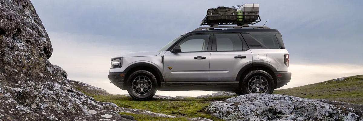 Shown is a 2022 Ford Bronco™ Sport parked on the grass near a rock wall and cargo is strapped to the roof