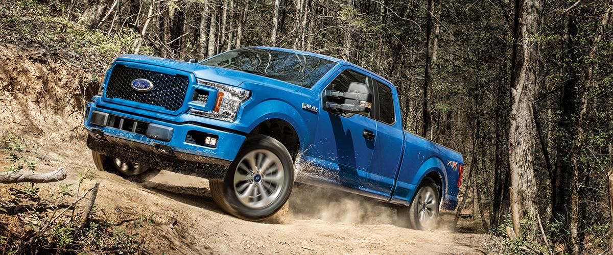 blue Ford F-150 pickup truck in the forest going up a mountain